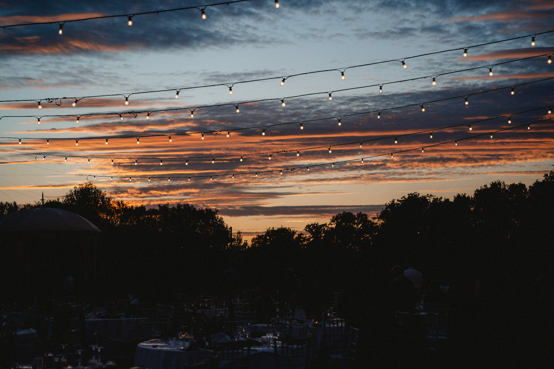 Luci a festoni al tramonto durante un ricevimento di matrimonio Gleam